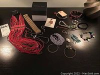 Overview of all costume jewelry including necklaces, bracelets, rings, and a Geoffrey Beene box on a dark surface