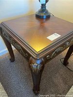 Close-up view of one Ashley Furniture square end table showing dark brown wood top with subtle finish pattern and carved legs with gold scrollwork detail.
