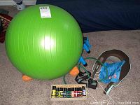 Photo shows green exercise ball, orange hand weights, neck massager device, essential oils box, and stretch band on floor