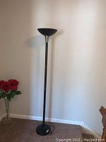 Full view of the black metal floor lamp showing its height and base on light colored wall background.