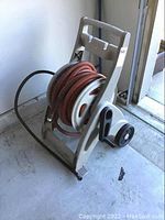Overall view of Suncast hose reel with orange hose coiled and mounted on wheels.
