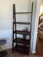 Full frontal view of dark wood ladder shelf standing against wall with five shelving tiers visible.