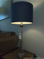 Lamp on side table with navy blue drum shade and glass/chrome base near brown couch