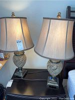 Pair of matte gold resin lamps with golden fabric lampshades shown side by side on a table, both with MaxSold tags.