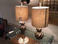 Pair of resin lamps with twisted bases and woven style shades on a glass table.