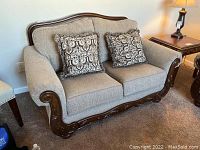 Front view of Ashley taupe loveseat with two patterned pillows and wooden frame base details.