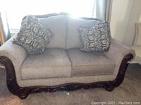 Front view of the taupe loveseat with wooden embellishments and two decorative throw pillows.