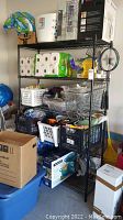 Full view of the shelving unit loaded with various items such as paper towels, baskets, boxes, fans, and household goods, showing the overall structure and black wire shelves.