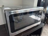 Full view of the microwave showing the silver stainless steel exterior and glass door with 'Sharp Carousel' logo.