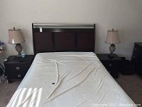Wide shot of the master bedroom featuring the bed and two matching Merlot color nightstands with two drawers each. Nightstands flanking the bed with lamps on top.