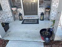 Front porch showing two black metal lanterns on each side of entrance, along with several plant stands and flower pots of various materials and sizes.