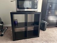 Photo showing espresso four cube shelf with a microwave on top, purple candle on left compartment and some items on right compartment. Shelf is empty inside compartments.