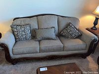 Full front view of Ashley Signature Furniture sofa with taupe cushions, wooden scrollwork base and three patterned throw pillows.