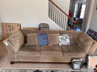 Front view of taupe brown micro suede sofa with three seat cushions and three back cushions, two decorative pillows placed on sofa, wooden base and legs visible.