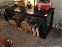Full side view of the rectangular table showing metal frame base and dark resin top with various household items on and underneath (not included in sale).