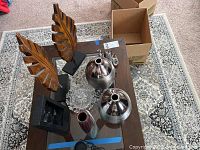 Overview of the wooden palm leaves on stands, two silver vases, small figurines, and crystal jar arranged on a table.