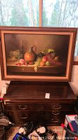 Front view of dark stained wooden cabinet with brass drawer pulls and scratches on top surface, a framed painting is visible above it.