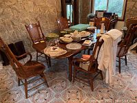 Photo of six wooden dining chairs around a dining table, showing full chairs with armrests and woven rattan backs in a rustic room.