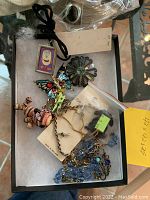 Assorted costume jewelry pieces in tray including brooches, pendants, necklaces