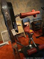 Side angle showing red padded arm rests, seat, black metal frame, and attached instruction poster stand.