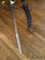 Longer sabre and leather sheath placed on wooden floor showing size and condition