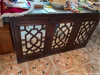 Full front view of wooden sideboard showing two mirrored cabinet doors with geometric lattice design and glass top with fabric on it.