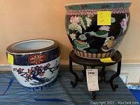 Two colorful ceramic vase bowls placed side by side on a table with a wooden vase stand supporting the black vase bowl.