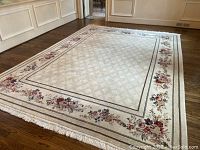 Full view of the hand-made Persian area rug laid on wood floor showing floral border pattern and central diamond background.