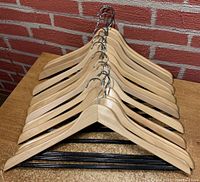 12 wooden hangers stacked together showing the metal hooks and wooden arms with black plastic rails.