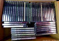 Top-down photo showing over 40 genealogy CDs packed in a cardboard box. CD cases are black with white text on the spines.