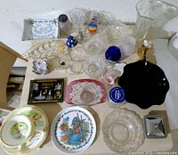 Top view of assorted glassware and dishware including clear crystal candy dishes, decorative plates, small glass bowls, salt shaker, and colorful glass items.
