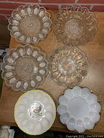 Top-down view showing all 6 egg plates arranged on table; glass and ceramic materials, different patterns and sizes