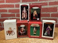 Photo showing six Hallmark Keepsake Santa ornaments in their original boxes, stacked in two rows with visible front and side artwork and labels.