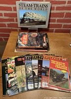 Photo showing a stack of steam and railroading books including Steam Trains of the World, To China For Steam, Railroad News magazines, and The Road to Paradise book.