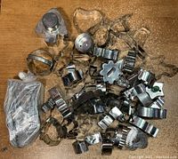 Photo showing a variety of vintage tin cookie cutters scattered on a surface including multiple shapes and a bag of additional cutters.