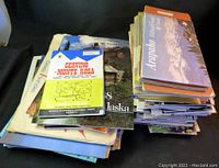 Wide view of two stacks of assorted travel pamphlets and maps on a dark surface
