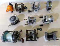 Top down view of all ten fishing reels laid out on table, showing variety in size, color, and style.