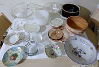 Various vintage kitchen bowls arranged on a table showing a mix of materials including glass, ceramic, porcelain, and wood, some with floral designs.