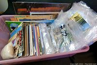 Photo showing large plastic tub filled with a large quantity of postcards with varied themes and sizes, some are plastic wrapped.