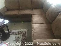 Photo of a large two-piece brown sectional sofa with cushions, showing the L-shaped arrangement and visible fabric texture and armrests.