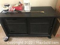 Black wooden TV storage cabinet with glass doors and two shelves inside, contents on top not included.