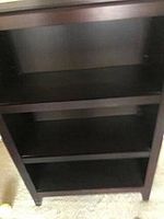 Black wooden bookcase with three shelves including two adjustable shelves visible, standing on carpet.