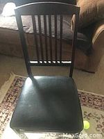 Front view of a black wooden chair with a slatted backrest and padded seat cushion.