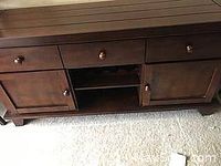 Frontal view of medium brown wooden storage cabinet showing three top drawers, two bottom door cabinets, and center space for wine bottles.