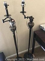 Photo showing two identical adjustable floor lamps with circular platforms and decorative urn shapes on tall metal stands.