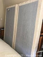 Two twin box springs standing side by side, beige fabric covering with light wear.