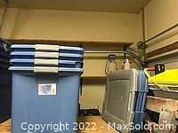 Photo showing 4 blue Sterilite plastic storage totes stacked with covers on top and nearby in a storage area.