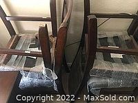 Four padded dining chairs arranged side by side showing wooden frames and gray fabric upholstery.