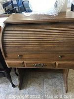 Wooden roll up desk with tambour roll-top closed, shows front view with metal hardware on drawers and wood finish.