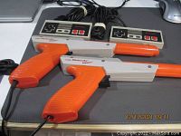 Photo showing two vintage Nintendo Zapper light guns and two original NES controllers laid on a desk surface.